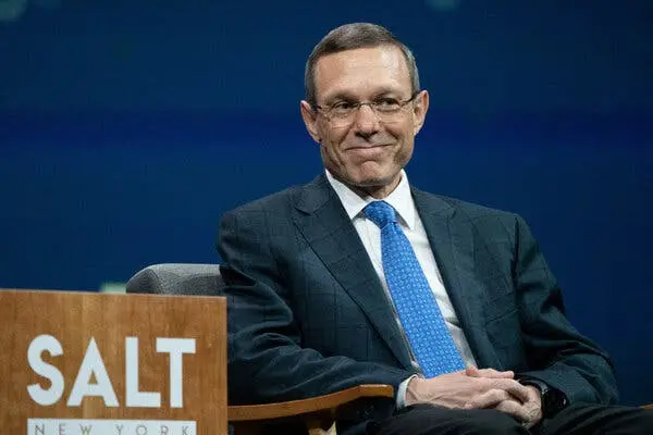 آوی لوب با کراوات و کت و شلوار لباس پوشیده و در حالی که روی صندلی در صحنه یک کنفرانس نشسته، لبخند میزند.