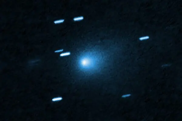 تصویر تلسکوپ فضایی از یک گوی آبی روشن دنبالهدار که از آسمان عبور میکند. ستارههای اطراف آن کمی تار هستند چون دوربین حرکت دنبالهدار را دنبال میکرد.