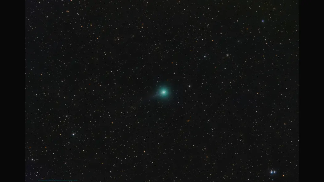 ستاره دنبالهدار سبز روشن در پایین سمت چپ یک میدان ستارهدار بر پسزمینهٔ سیاه، با دم طولانی که به سمت بالا‑راست صفحه گسترش مییابد