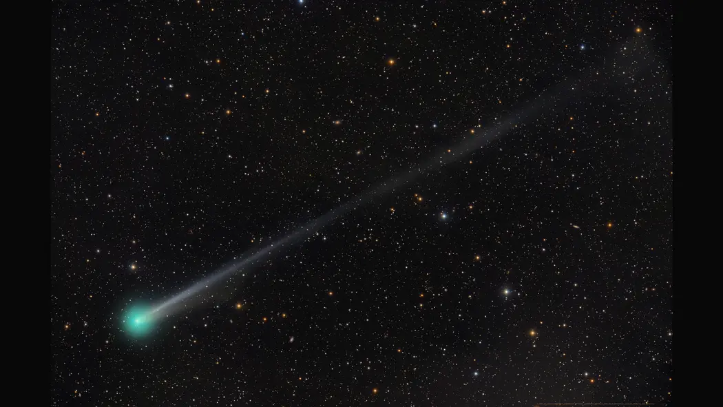 ستاره دنبالهدار سبز روشن در پایین سمت چپ یک میدان ستارهدار بر پسزمینهٔ سیاه، با دم طولانی که به سمت بالا‑راست صفحه گسترش مییابد
