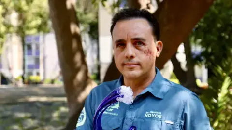 ماوریسو هوئوس در حال نگاه به دوربین است، در حالی که جایزهای به شکل موج در دست دارد