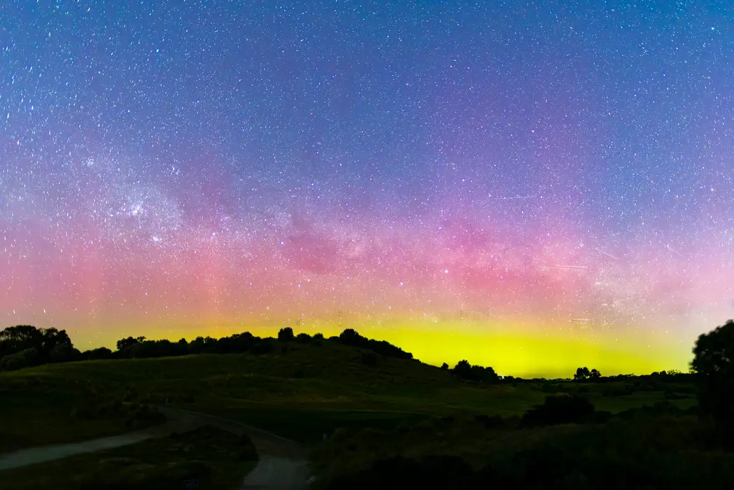 نوارهای نور زرد و بنفش که در پسزمینهٔ ستارگان و افق سیلوئتی دیده میشوند