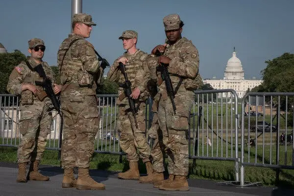 سربازان گارد ملی در لباس یکنواخت، جلوی حصارها ایستادهاند؛ کاخ سفید در پسزمینه دورتر دیده میشود.
