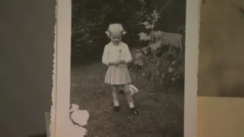 عکس ارسالی: تصویر سیاهوسفید لانا پونتینگ بهعنوان دخترک. او در پیراهن رنگ روشن است و موهای کوتاه بلوندش در شاخکها بستهاند.