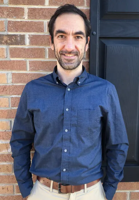 مردی با پیراهن آبی در برابر دیوار آجری.