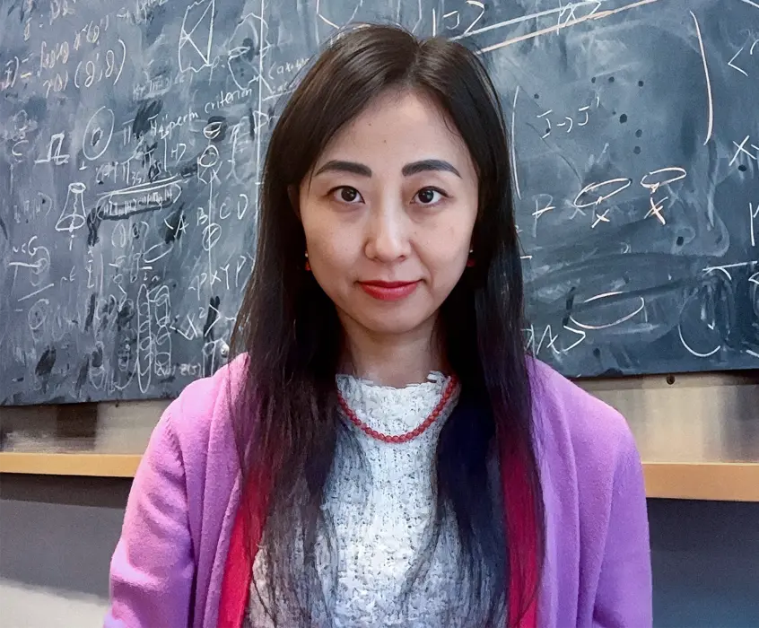 زنی با پلیور صورتی جلوی تخته سیاه.