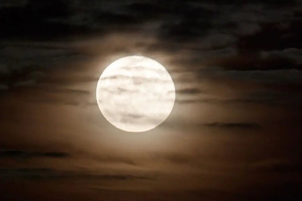 ماه کامل در آسمان شب که تا حدی توسط ابرها پوشیده شده است