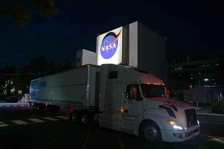 یک کامیون بزرگ در حال عبور از ساختمان حاوی لوگوی توپی ناسا